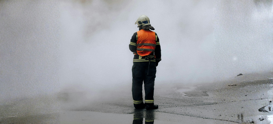 First responder in gear standing in front of white smoke}