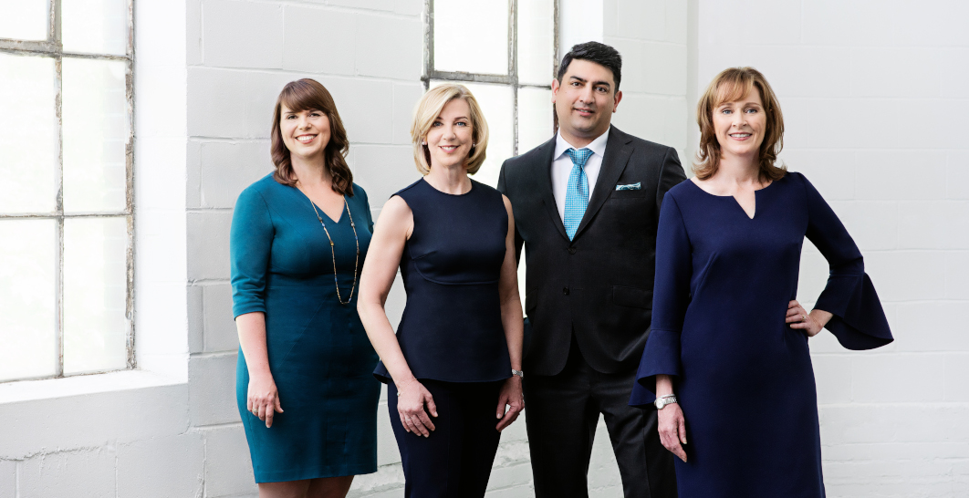 The Four Founding Partners Stand Together Wearing Blue in a White Room