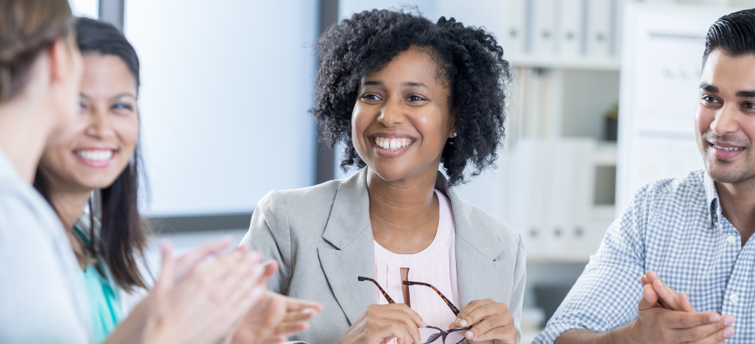 A woman in a board room with her colleagues being applauded 