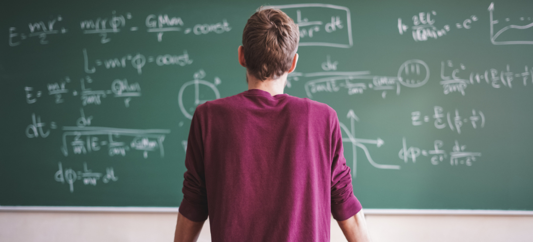 A student stands in front of a chalkboard, reading formulas 