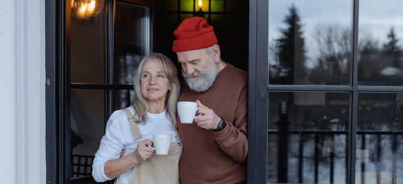 a retired couple looking outside through patio doors while drinking coffee